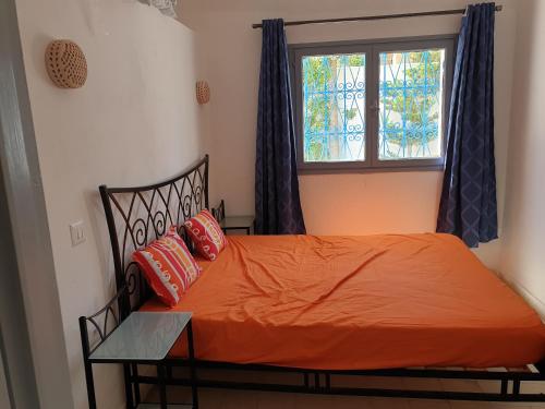 a bedroom with a bed with an orange sheet and a window at Chelly Bungalow en bord de mer in Nabeul