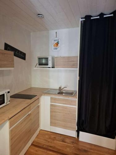 - une cuisine avec un évier et un rideau noir dans l'établissement le nid des choups le petit duplex 2 personnes, à La Bourboule