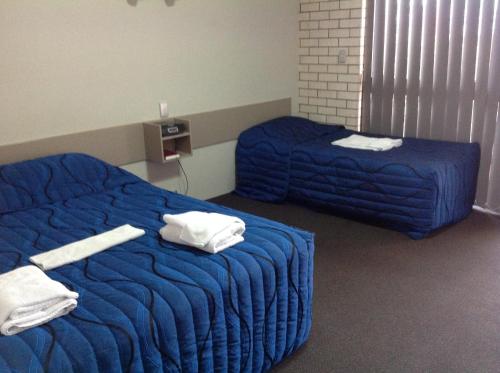 two beds in a room with blue sheets and towels at Tannum Sands Hotel / Motel in Tannum Sands