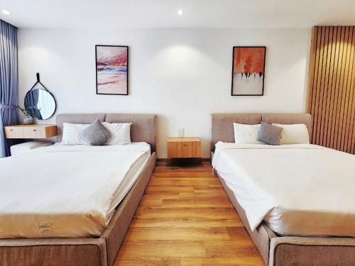 two beds in a room with white walls and wooden floors at TMS Quy Nhơn - RUBY Luxury Apartment in Quy Nhon