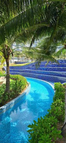 a blue swimming pool with a palm tree and bushes at Arena jakovi condotel in Cam Ranh
