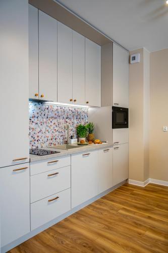 a white kitchen with white cabinets and wood floors at Oasis Apartment Strzelecka 57 in Bydgoszcz