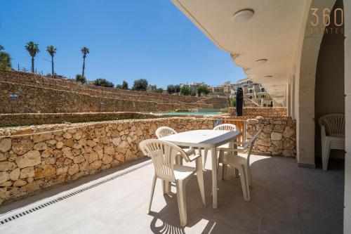a table and chairs on a patio with a stone wall at Serene Apt with Terrace & Pool & BBQ Access,Qala by 360 Estates in Qala
