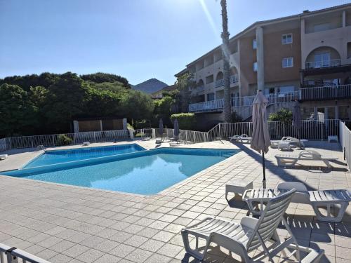 - une piscine avec des chaises et un parasol à côté d'un bâtiment dans l'établissement SAINT FLORENT - 3 Pièces dans résidence avec piscine, à Saint-Florent