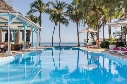 a swimming pool with palm trees and the ocean at Cocotiers Hotel – Mauritius in Port Louis
