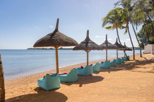 a row of straw umbrellas on a beach at Cocotiers Hotel – Mauritius in Port Louis
