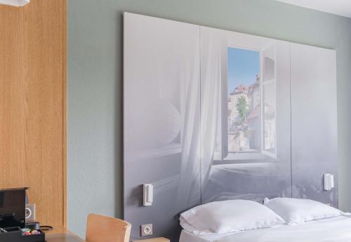 a bedroom with a white bed and a window at B&B HOTEL Besançon Chateaufarine in Besançon
