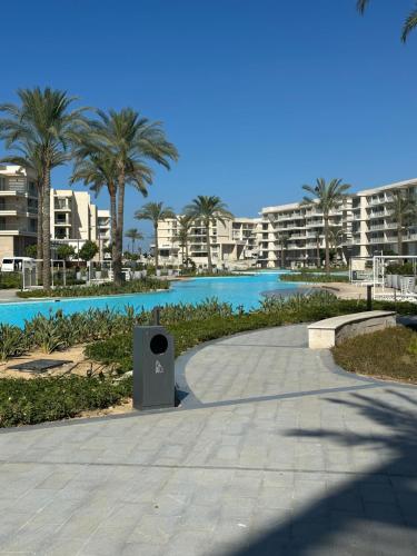 einen Fußweg neben einem Pool mit Palmen und Gebäuden in der Unterkunft Marassi 2-bed Marina Views Sandy Lagoon in El-Alamein