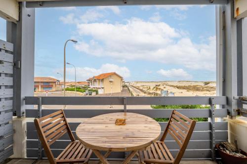 un tavolo in legno e 2 sedie seduti su un balcone di Appartement au pied des dunes avec vue a Biscarrosse