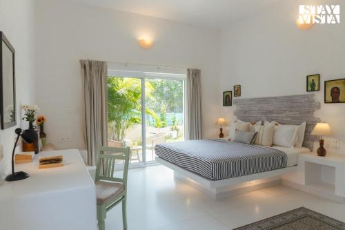 a bedroom with a bed and a desk and a window at Aroha Palms Luxury Villas in Mandrem