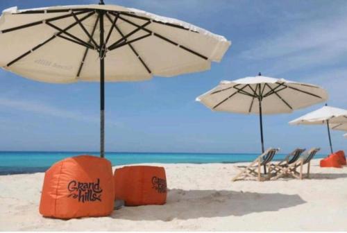 two umbrellas and chairs on a sandy beach at chalet with garden in grand view I06 in Dawwār ‘Abd Allāh