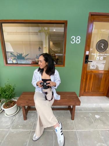 a woman sitting on a bench holding a camera at Round The Clock Hostel in Samphanthawong