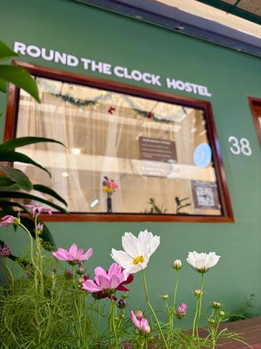 a window of a store with flowers in front of it at Round The Clock Hostel in Samphanthawong