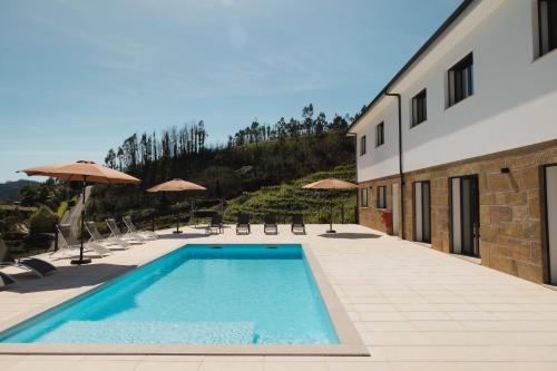 a swimming pool next to a building with chairs and umbrellas at Casa do Tojo (Camélias de Basto - Turismo Rural) in Pedras Alvas