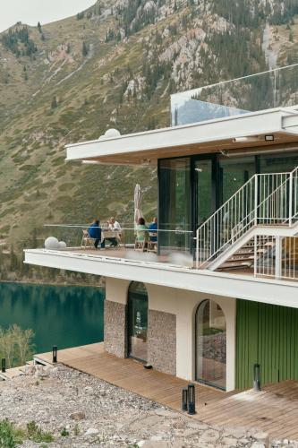 a building with people sitting on a balcony next to a mountain at Pana Unique Kolsay in Kurmenty
