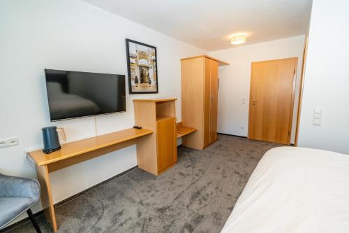 a room with a bed and a desk with a television at Hotel Grado in Ransbach-Baumbach