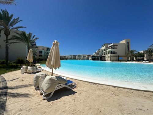 a beach with chairs and an umbrella and a pool at Marvelous 2BR with Garden in Marassi, Blanca Lagoons in El Alamein