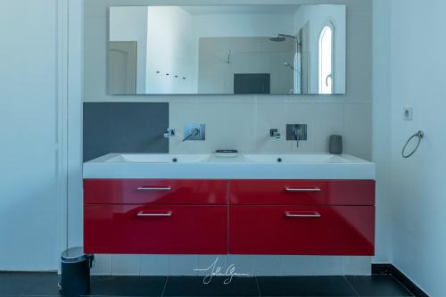 La salle de bains est pourvue de placards rouges et d'un lavabo blanc. dans l'établissement Villa des Chardonnerets, à Mougins
