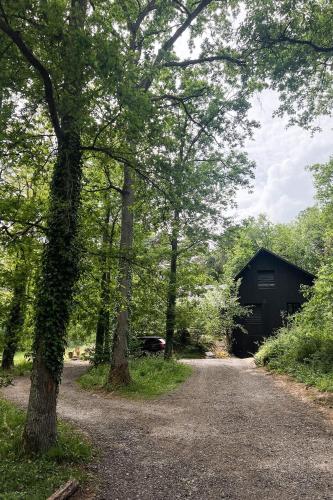 un chemin de gravier menant à une grange noire avec des arbres dans l'établissement Maison de Reve avec Sauna en Pleine Foret, à Le Vaudoué