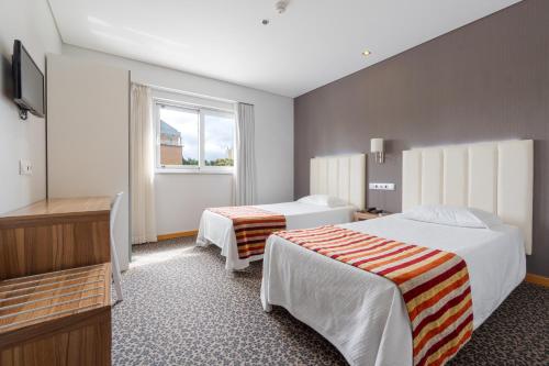 Una habitación de hotel con dos camas y una ventana. en Hotel Azinheira by RIDAN Hotels, en Fátima