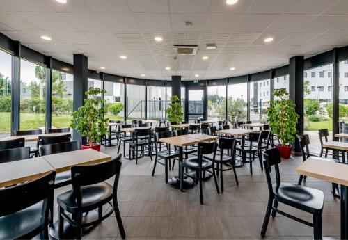 a restaurant with tables and chairs and windows at B&B HOTEL Bordeaux Est 3 étoiles in Tresses