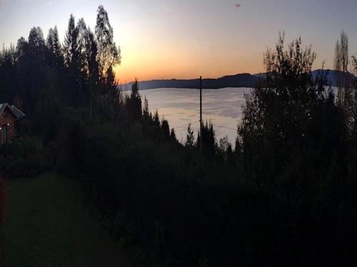 a sunset over a lake with a house and trees at Cabanas Mapulauquen in Pucará