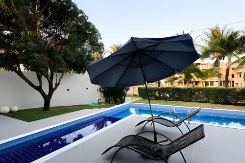 a chair and an umbrella next to a swimming pool at Casa Praia de Sonho Verde condomínio fechado in Paripueira