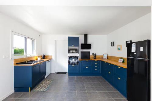 - une cuisine avec des armoires bleues et un réfrigérateur noir dans l'établissement Maison neuve à deux pas de la plage et du GR34, à Pleubian