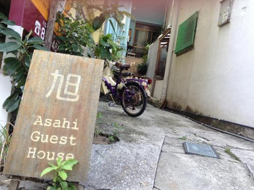 um sinal para uma casa de hóspedes ao lado de uma bicicleta em Asahi Guest House em Naha