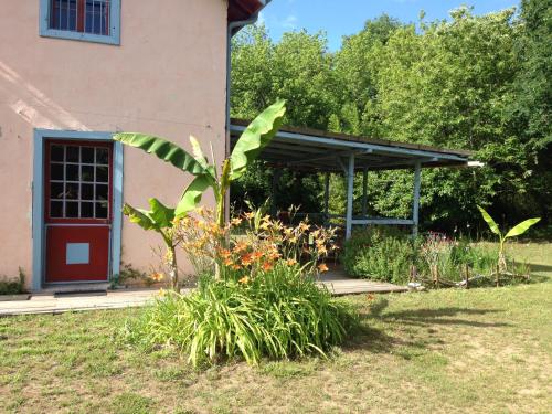 un jardin en face d'un bâtiment avec une porte rouge dans l'établissement Maison ancienne dans parc boisé, à Magescq