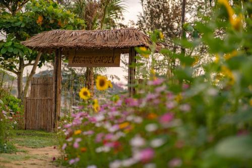 a sign in a garden with a thatch roof at Crown Retreat Quy Nhon Resort in Quy Nhon