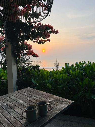 two coffee mugs sitting on a table with the sunset at Crown Retreat Quy Nhon Resort in Quy Nhon