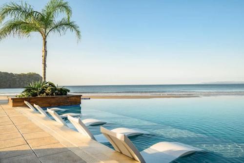 a swimming pool with white chairs and a palm tree at Private PentHouse H Sea Views Style & Serenity in Blue Venao in Playa Venao