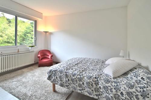 - une chambre blanche avec un lit et une chaise rouge dans l'établissement Havre familial standing Jardins Vue, à Marly-le-Roi