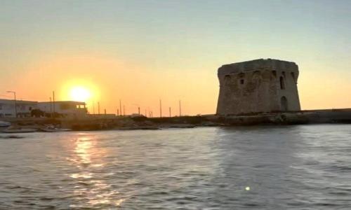 a building in the water with the sunset in the background at Aurora e Alba in Casalabate