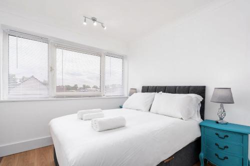 a bedroom with a white bed with a blue nightstand and windows at Chic 3 BR Home with Balcony & Free Parking in Leeds