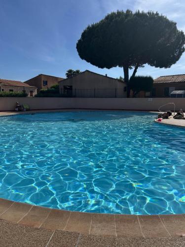 una gran piscina azul con un árbol en el fondo en Mazet climatisé avec piscine & tennis Résidence calme proche Lavandou, en Bormes-les-Mimosas