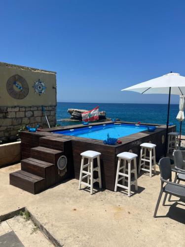 a swimming pool with chairs and an umbrella next to the ocean at Golden Stone Beach in Halat Byblos