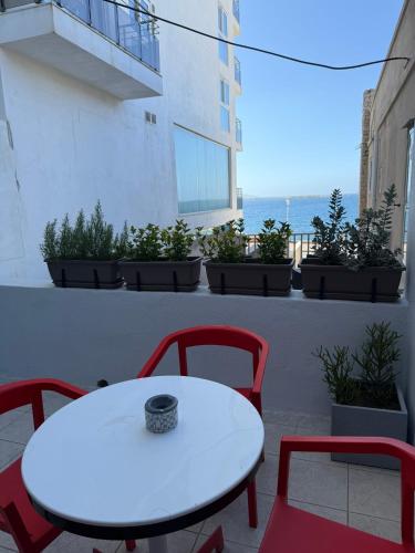 a white table and red chairs on a balcony with the ocean at Camelia - 3 Bedroom Maisonnette with terrace and Seaviews - Bugibba in St Paul's Bay