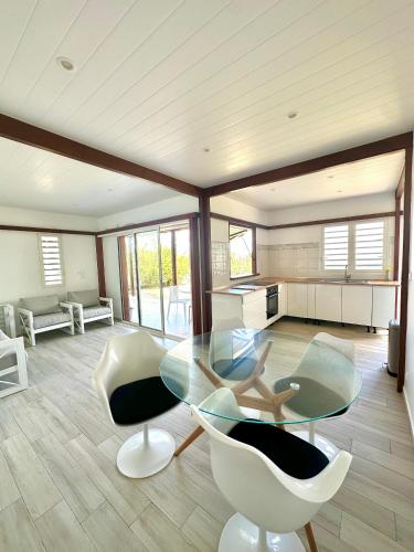 a dining room with a glass table and white chairs at Villa " Une Histoire", votre havre de paix à deux pas de la plage in Sainte-Rose