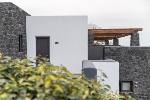 a white house with a black door and a stone wall at Brilliance Suites in Imerovigli