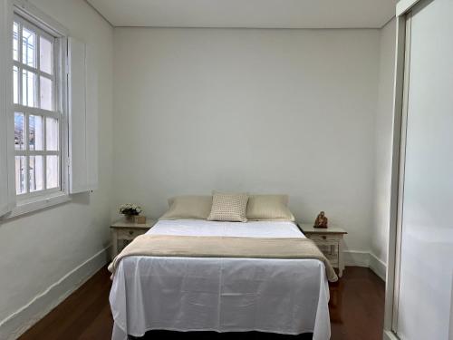 une chambre blanche avec un lit et deux fenêtres dans l'établissement Casa Zara, à Diamantina