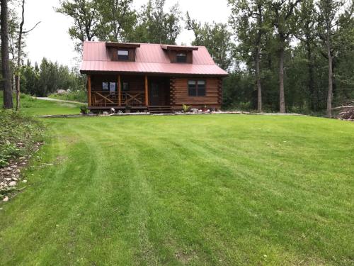 a log cabin with a red roof on a green field at Alaska's Harvest Bed and Breakfast and Luxury Log Cabin in Palmer