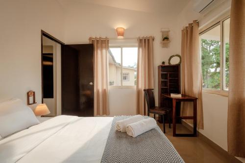 a bedroom with a bed and a desk and a window at CasaKai 2BHK Bohemian Spread with 3 Patios & Pool, Near Thalassa in Siolim