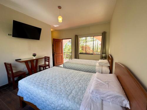 a bedroom with two beds and a desk and a television at Casa Hotel Mamaluna in Lunahuaná