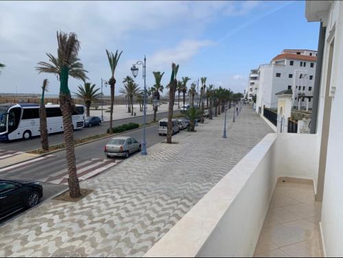 a sidewalk with palm trees and a street with cars at Zellaka Apartamento Vista al mar in Asilah