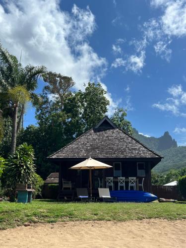 a house with an umbrella and chairs and a boat at Bungalow Plage Bobby - Moorea Dolphin Lodge in Moorea
