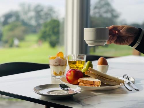 a person holding a coffee cup over a plate of food at The Select Inn Ryde in Sydney
