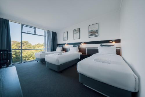 a hotel room with three beds and a large window at The Select Inn Ryde in Sydney