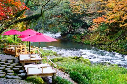 a group of tables with pink umbrellas next to a river at Yamanaka Onsen Kajikaso - Opening in 1st, Aug 2025 in Kaga